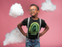 products/black-kid-wearing-a-t-shirt-mockup-and-glasses-while-standing-in-a-pink-room-with-clouds-a19727.png